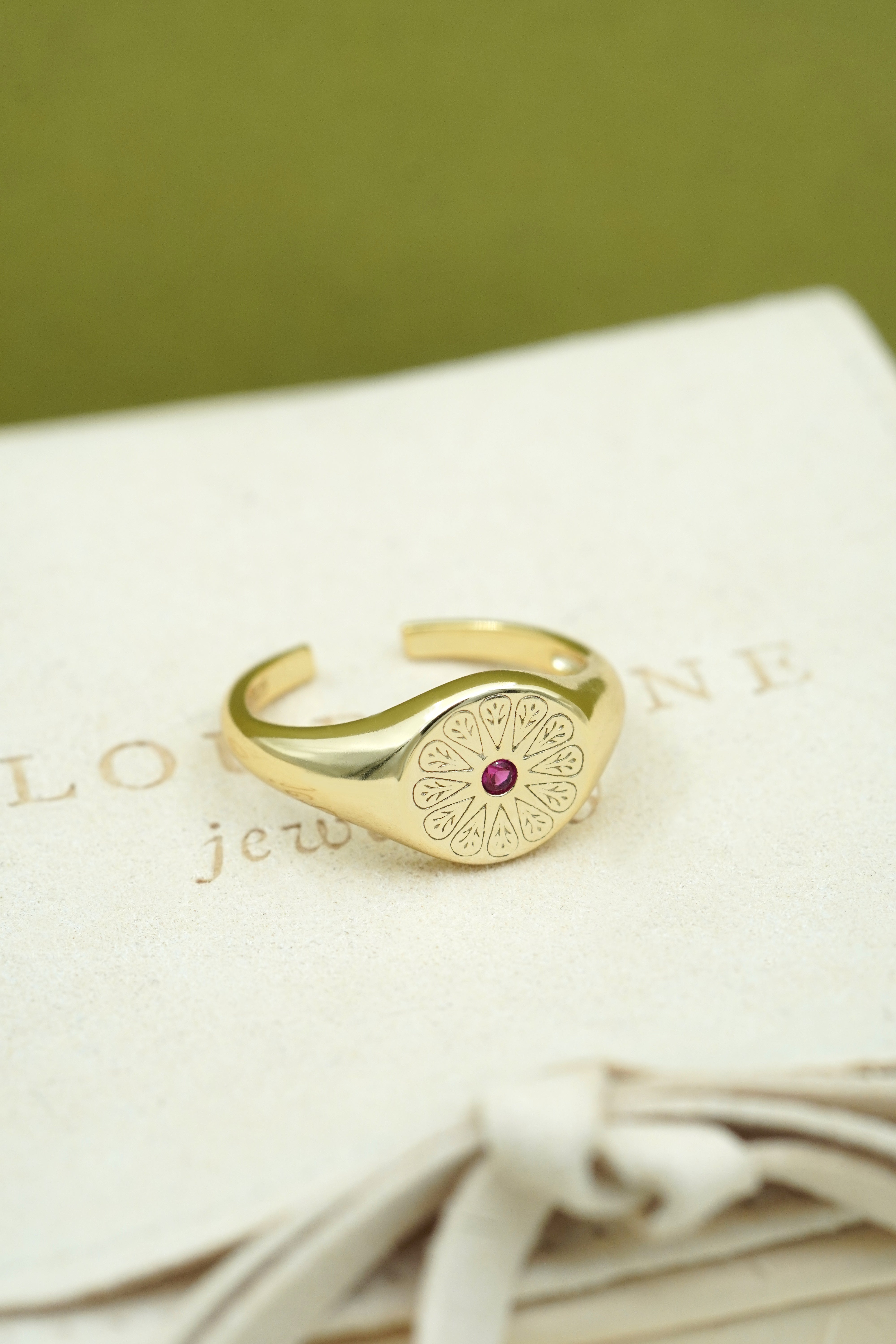 Gold July Ruby Signet Birthstone Ring on cream fabric