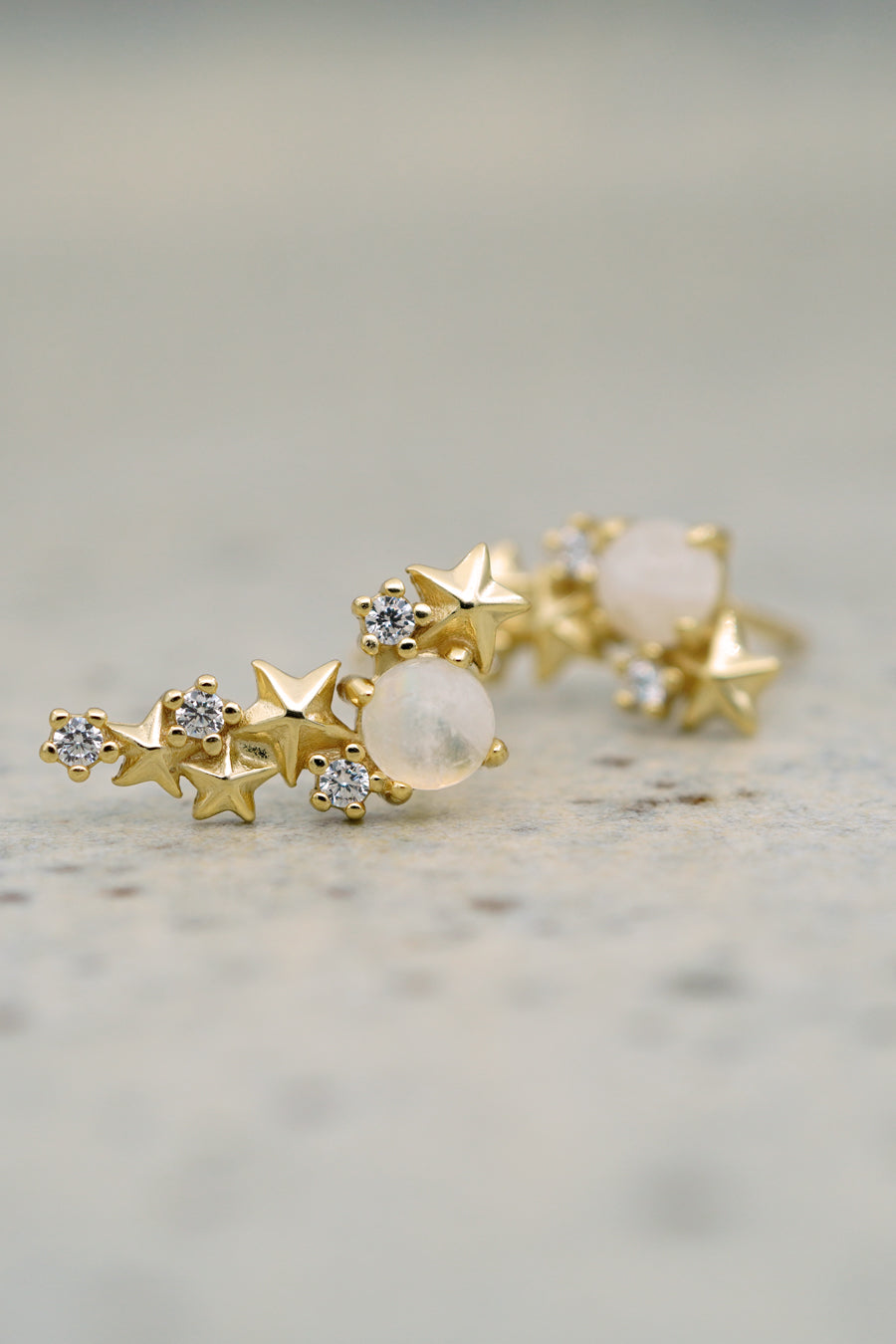 Gold Matariki Earrings jewellery on pale blue background